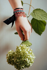 a bracelet of beads and black ribbon on the hand of a girl holding a flower 
