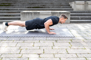 Sportive young man doing push-ups on concrete background outdoors.