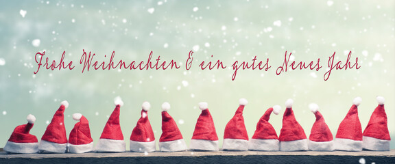 Hats of Santa in a row on a rustic wooden table with the German words Merry Christmas and a happy...