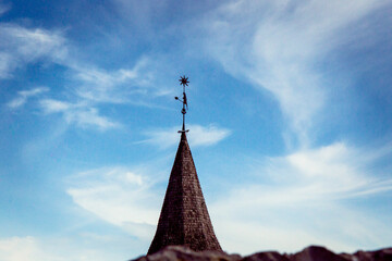 metal weather vane on the roof of the house against the background of the blue sky 