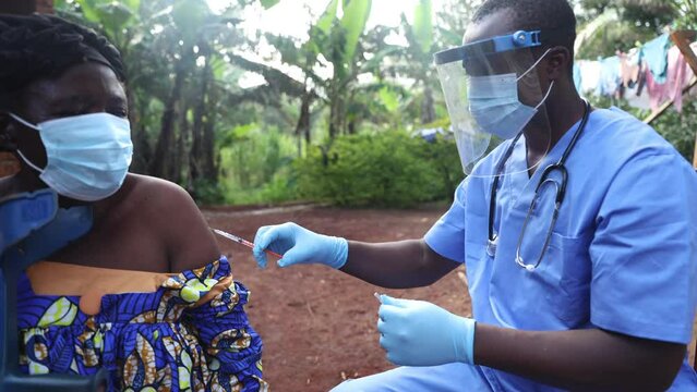 A doctor vaccinates an elderly patient with a syringe in an African village.