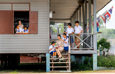 Woman teacher teach and train her student in area of steps of the building with some student also look through the window and they look happy at school.
