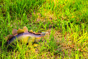 Toy dinosaur in tall green grass in the garden.