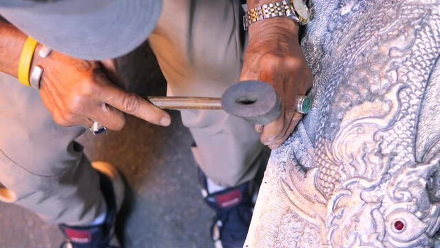 Talented blacksmith at work, using traditional tools like hammer and chisel making design on metal sculpture, high quality cinematic 4K traditional asian craftsman at work footage, Thailand.