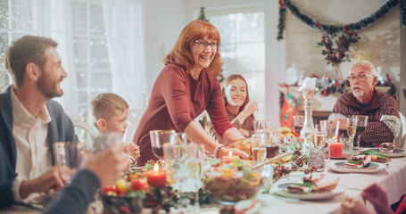 Diverse Group of Relatives and Friends Sitting Together Behind a Dining Table with Tasty Meals and Festive Decorations. Senior Woman Bringing a Grilled Chicken, Creating a Joyful Holiday Atmosphere