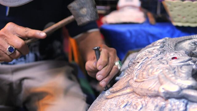 Talented blacksmith at work, using traditional tools like hammer and chisel making design on metal sculpture, high quality cinematic 4K traditional asian craftsman at work footage, Thailand.