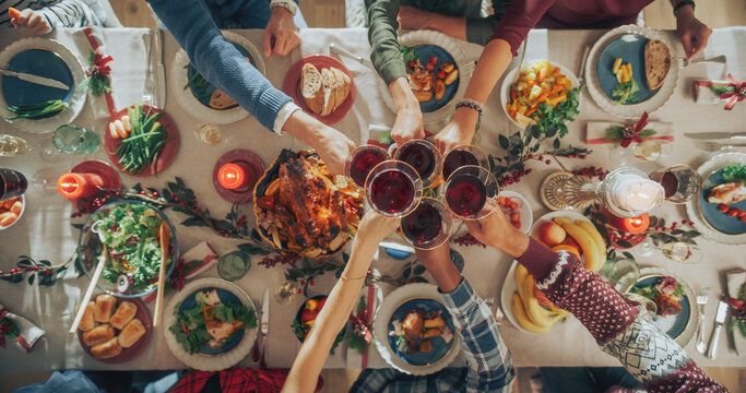 Parents, Children and Friends Enjoying Christmas Dinner Together in a Cozy Home. Relatives Sharing Meals, Raising Glasses with Red Wine, Toasting, Celebrating a Holiday. Top Down View