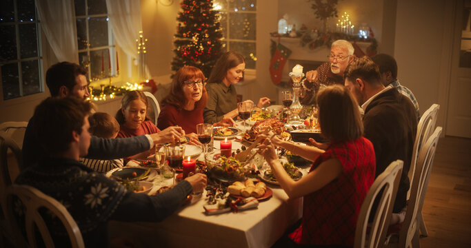 Diverse Group of People, Young and Old, Share a Joyful Christmas Dinner at Home. Family Sitting Behind a Big Dining Table Full of Delicious Food with Roast Turkey Feast. High Angle Evening