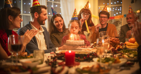 Naklejka na ściany i meble Young Handsome Father Bringing a Birthday Cake with Candlelights to His Cute Daughter. Excited Girl Blowing Out Candles and Making a Wish at a Family Dinner Celebration at Home