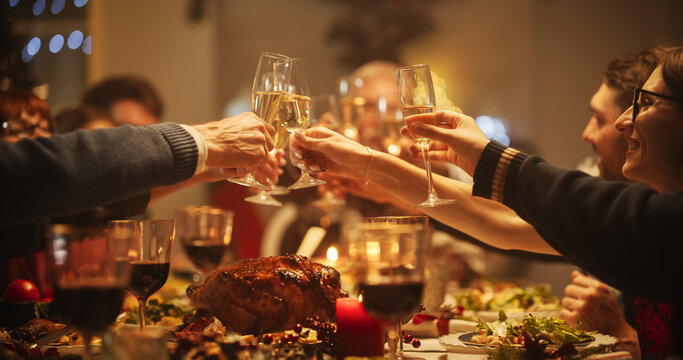 Family, Children And Friends Spend Christmas Dinner Together At Home In The Afternoon. Multicultural Family Raising And Clinking Champagne Glasses, Celebrating A Holiday With A Delicious Turkey Meal