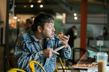 Close up focus view of bearded young man eating a slice of hot delicious pizza with tomato and...