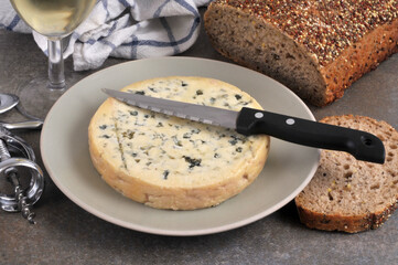 Fourme d'Ambert dans une assiette avec un couteau et du pain aux graines et un verre de vin