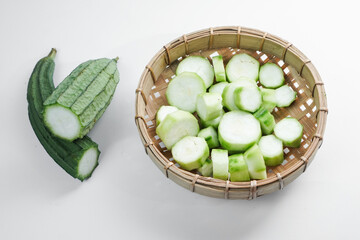 Pieces of Gambas or raw Gourd, Luffa Acutangula in a bamboo container. Isolated white background.
