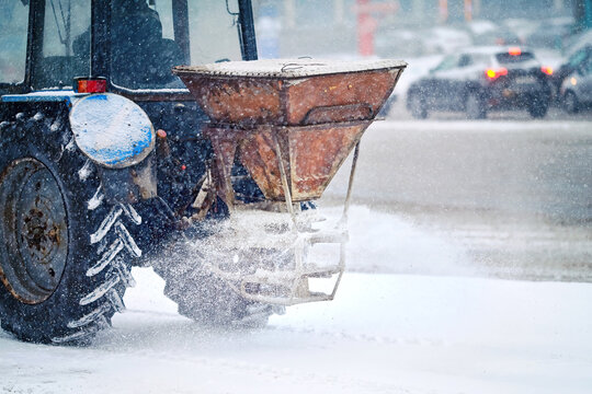 Tractor with salt bucket spread salt, deicing street. Utility vehicle melt ice. Tactor spreading with salt spreader sptinkle sidewalk during snow storm, winter road maintenance, prevent slipping.