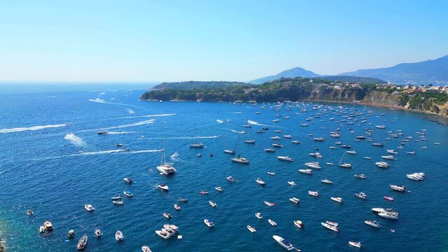 Inspiring aerial truck right shot from Panoramica sulla Corricella on Procida Island (Isola di Procida) sidetracking white boats cruising the wavy blue Tyrrhenian Sea and leaving wakes amongst slopes