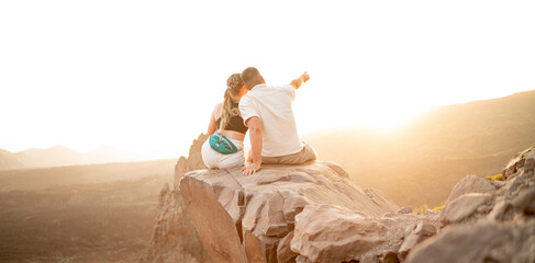 Pärchen sitzt nach einer langen Wanderung auf einem großen Felsen und genießt einen atemberaubenden Ausblick