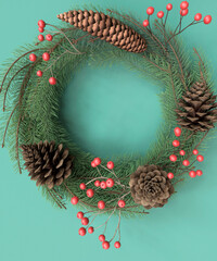 Ornate Christmas wreath with pine cones and re holly berries on a turquoise background 3d render