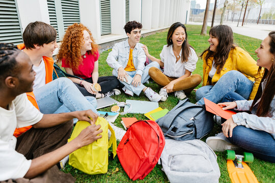 College Student Group Sitting Together At Campus Grass. Diverse Millennial Classmates Relaxing After Class Outdoors. Friendship And Education Lifestyle Concept.