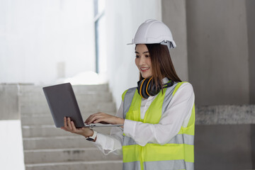 Asian construction worker woman using laptop at the construction site, industrial building design project concept. 