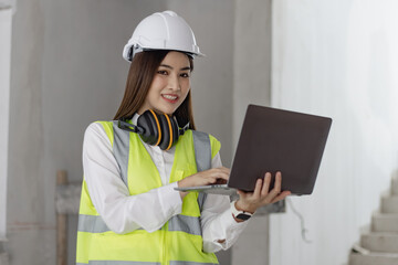 Asian construction worker woman using laptop at the construction site, industrial building design project concept. 