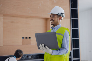 Asian construction worker using laptop at the construction site, industrial building design project concept. 