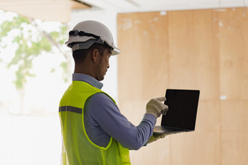 Asian construction worker using laptop at the construction site, industrial building design project concept. 