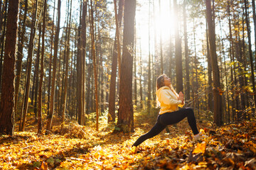 Active woman practices yoga in the autumn forest among yellow fallen leaves, catches zen. Concept...