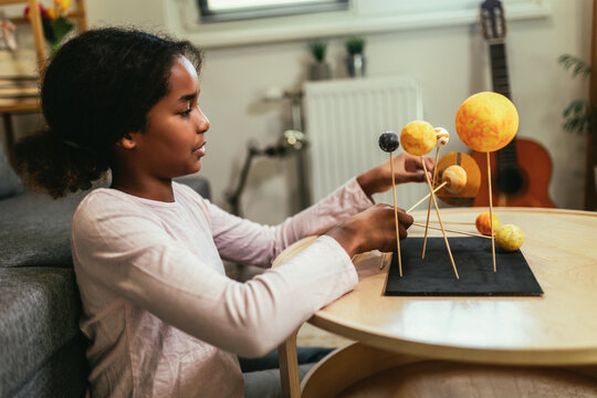 Happy african american school girl making a solar system for a school science project at home