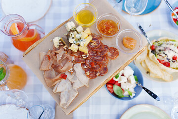 Wooden tray with assorted meats and cheeses with sauces.