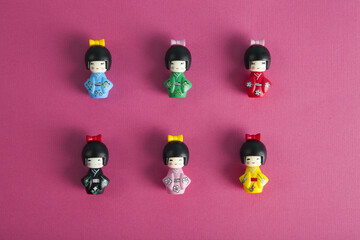 a collection of 6 wooden kokeshi dolls aligned in rows and columns on a fushia background