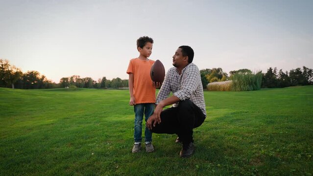 Father teaching son playing american football on green lawn