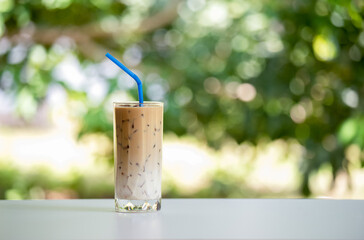 Iced coffee on white table, green background. Cold beverage in summer.