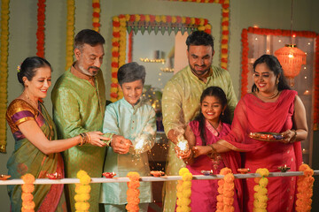 Group of family member enjoying by seeing kids playing with sparklers or fireworks during diwali festival celebration at home - concept of Happy Moments, traditional culture and reunion