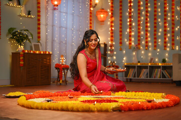Happy young Indian woman placing diya lamps on decorated flower rangoli for diwali festival...