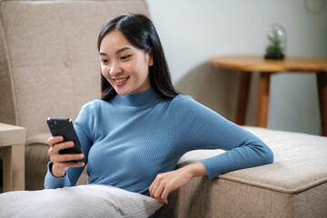 Smiling woman holding smartphone and banking credit card, involved in online mobile shopping at home, happy female shopper purchasing goods or services in internet store.