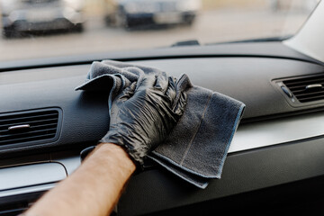 Man's hand in black glove cleaning car interior, dashboard and leather seats with microfiber cloth....