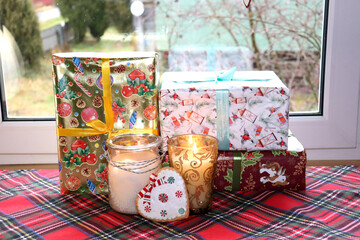 Christmas gifts in boxes and burning candles in glass candlesticks near the window, horizontal photo, close-up