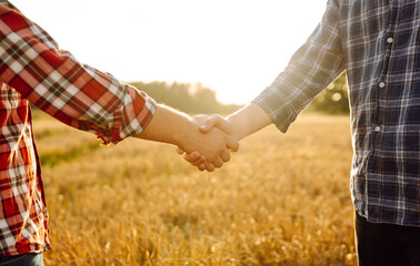 Against the backdrop of a golden wheat field, two farmers shake hands. Successful businessmen...