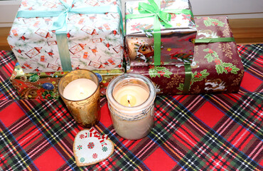 Christmas gifts in boxes and burning candles in glass candlesticks with gingerbread on a crucian checkered tablecloth, horizontal photo, top view