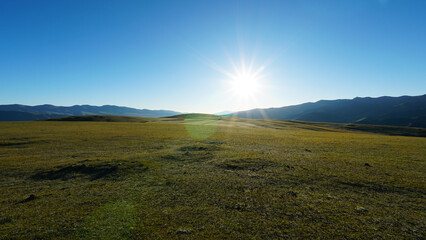Sunrise with a view of green hills and snowy peaks. Spacious green fields and yellow grass in...
