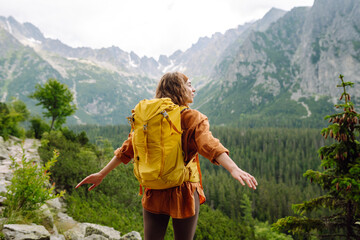 Smiling traveler with a bright backpack on a hiking mountain trail. A beautiful woman on a cliff...