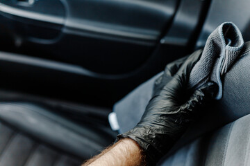 Man's hand in black glove cleaning car interior, dashboard and leather seats with microfiber cloth. Hand wipe down suede leather seat saloon interior.