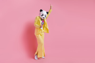 Full length of cool carefree person 3d panda mask point finger sing microphone empty space isolated on pink color background © deagreez