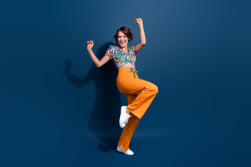 Full body photo of pretty young girl raise fists celebrate winning wear trendy flared pants outfit isolated on dark blue color background
