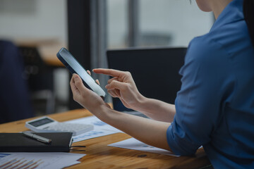 Asian businesswoman using smartphone sitting at desk in office, working online, 