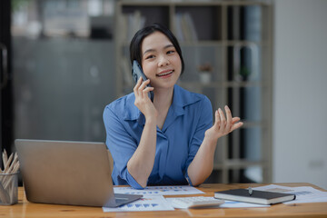 Asian businesswoman using smartphone sitting at desk in office, working online, 