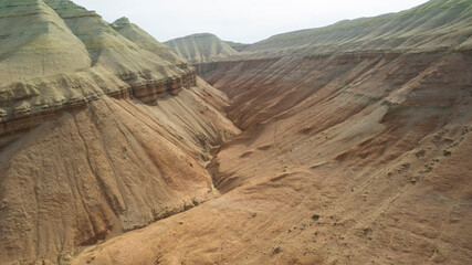 Colorful high mountains and a canyon made of clay. A large gorge with different rocks and different colors. Red, orange, white and yellow flowers of the walls of the rocks. A tourist walks. Aktau