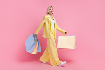 Full length profile photo of stunning cheerful person hold store bags walking isolated on pink color background