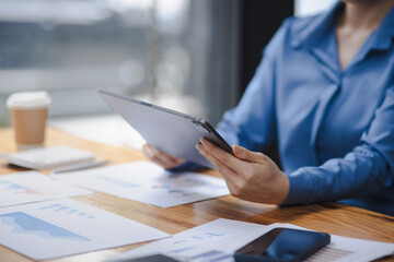 Asian woman working with document papers and tablet sitting at desk workplace office.