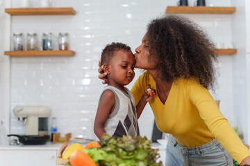 Happy African mother and son making salad while preparing food in the kitchen having fun, mother and son cooking activity concept.